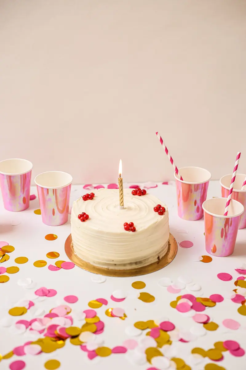 Liten hvit bursdagskake med lys, konfetti og rosa krus