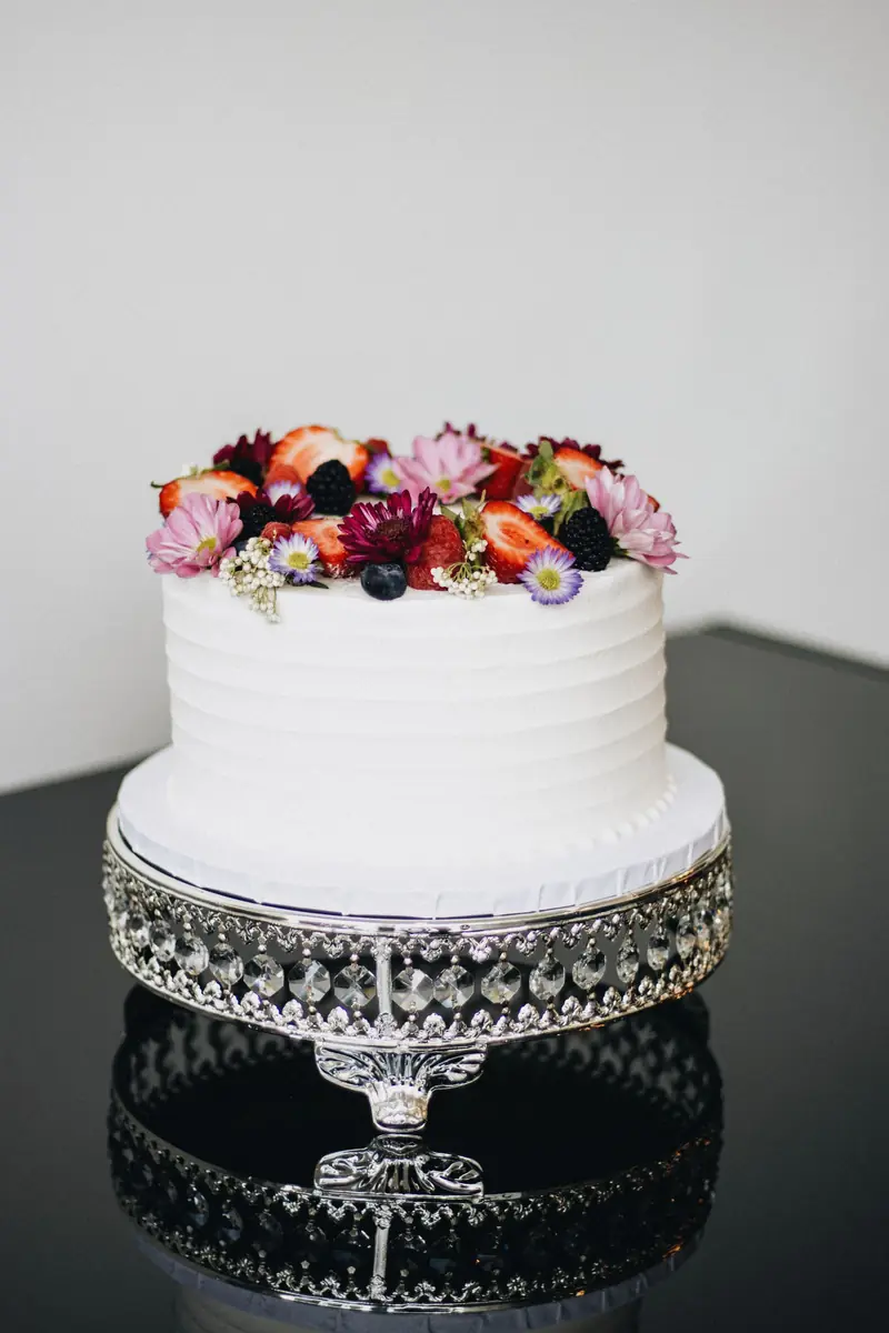 Hvit kremkake med friske blomster og bær på kakefat